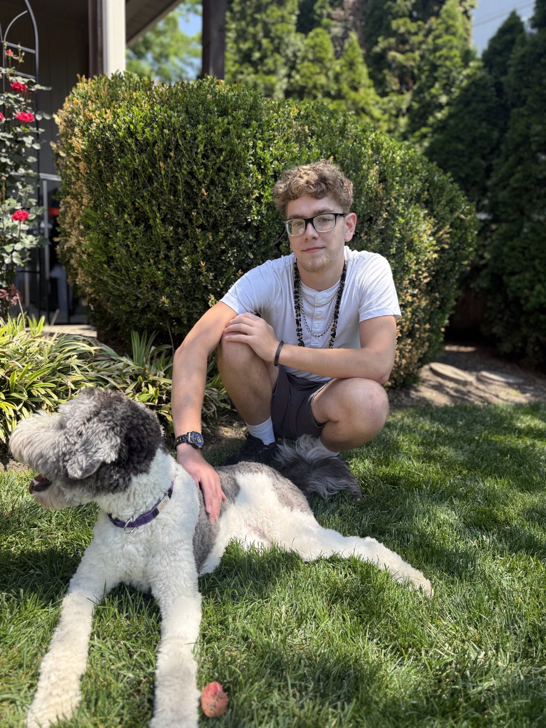 Ethan kneels beside a large, gentle dog in the grass — one hand on its back, a quiet attention between them.